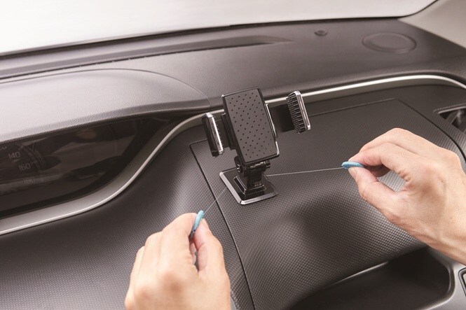 取り外し用ツールを使い、車のダッシュボードからスマートフォンホルダーを外し、スコッチ™ 車内用超強力両面テープを丁寧にはがしている様子
